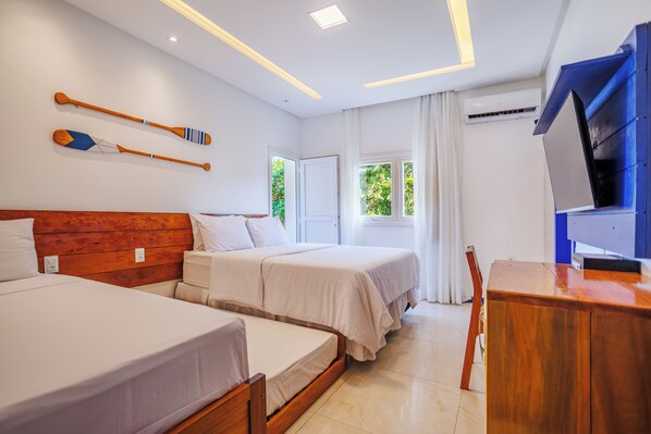 Quarto de hotel com duas camas, cabeceira de madeira, escrivaninha e televisão.