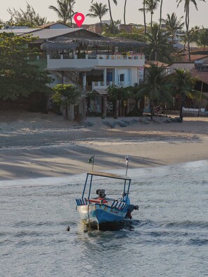 Un bote sobre aguas tranquilas cerca de una playa con edificios y palmeras al fondo.