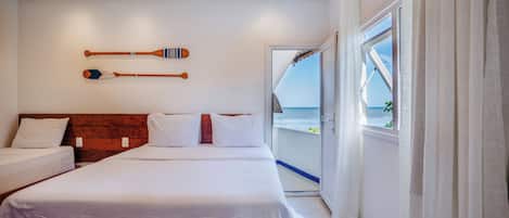 Habitación de hotel con cama, cabecera de madera, vista al mar por la ventana y dos palas de madera en la pared.