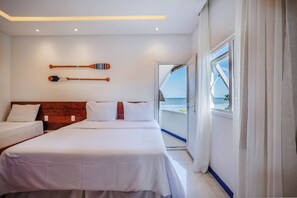Quarto de hotel com cama, cabeceira de madeira, vista para o mar pela janela e dois remos de madeira na parede.