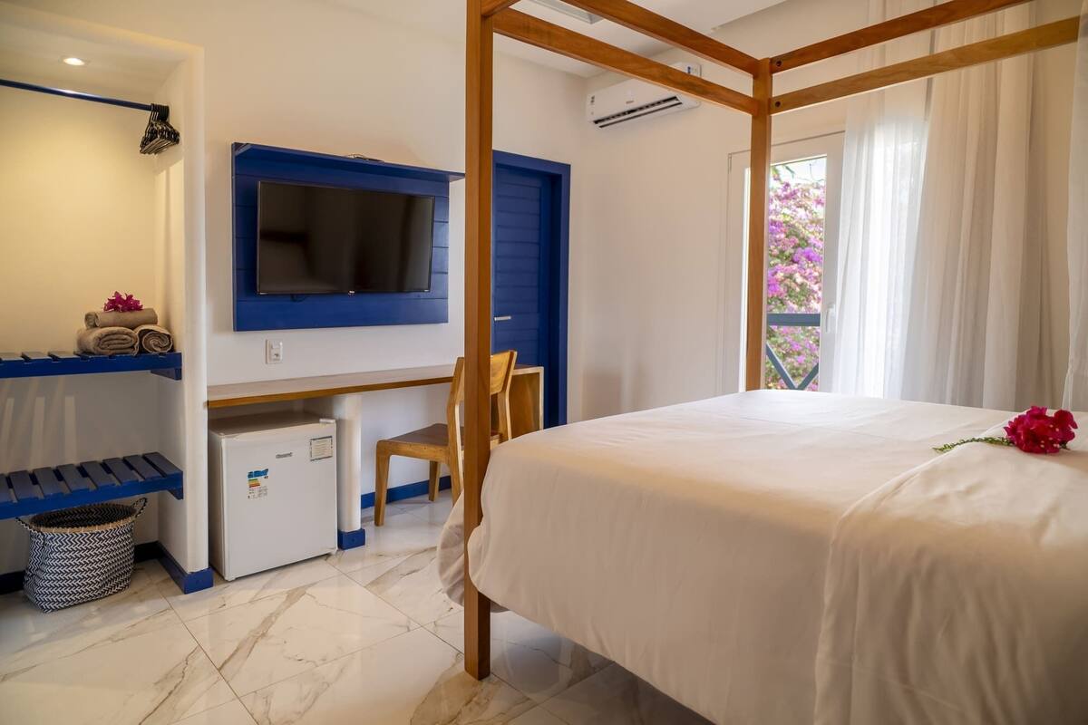 Une chambre à coucher comprenant un lit, un bureau avec un ordinateur, une chaise, un petit réfrigérateur et une fenêtre avec des rideaux.
