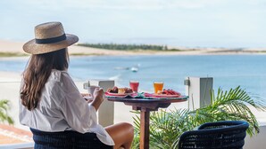 Una persona sentada a una mesa con vista al mar, un plato de comida y bebidas.