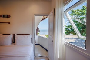 Un dormitorio con cama, ventana con vista a la playa y puerta que da al exterior.
