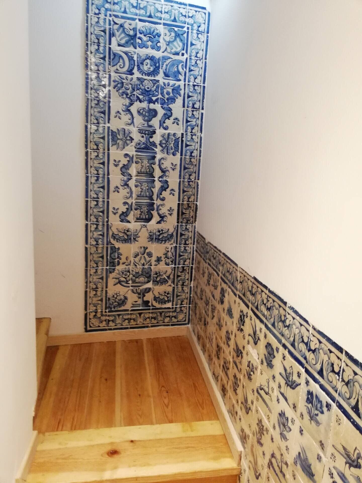 Una escalera con baldosas azules y blancas de diseño en las paredes y escalones de madera.