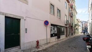 A narrow cobblestone street with a pink building featuring a green door, a red fire hydrant, and a no parking sign.