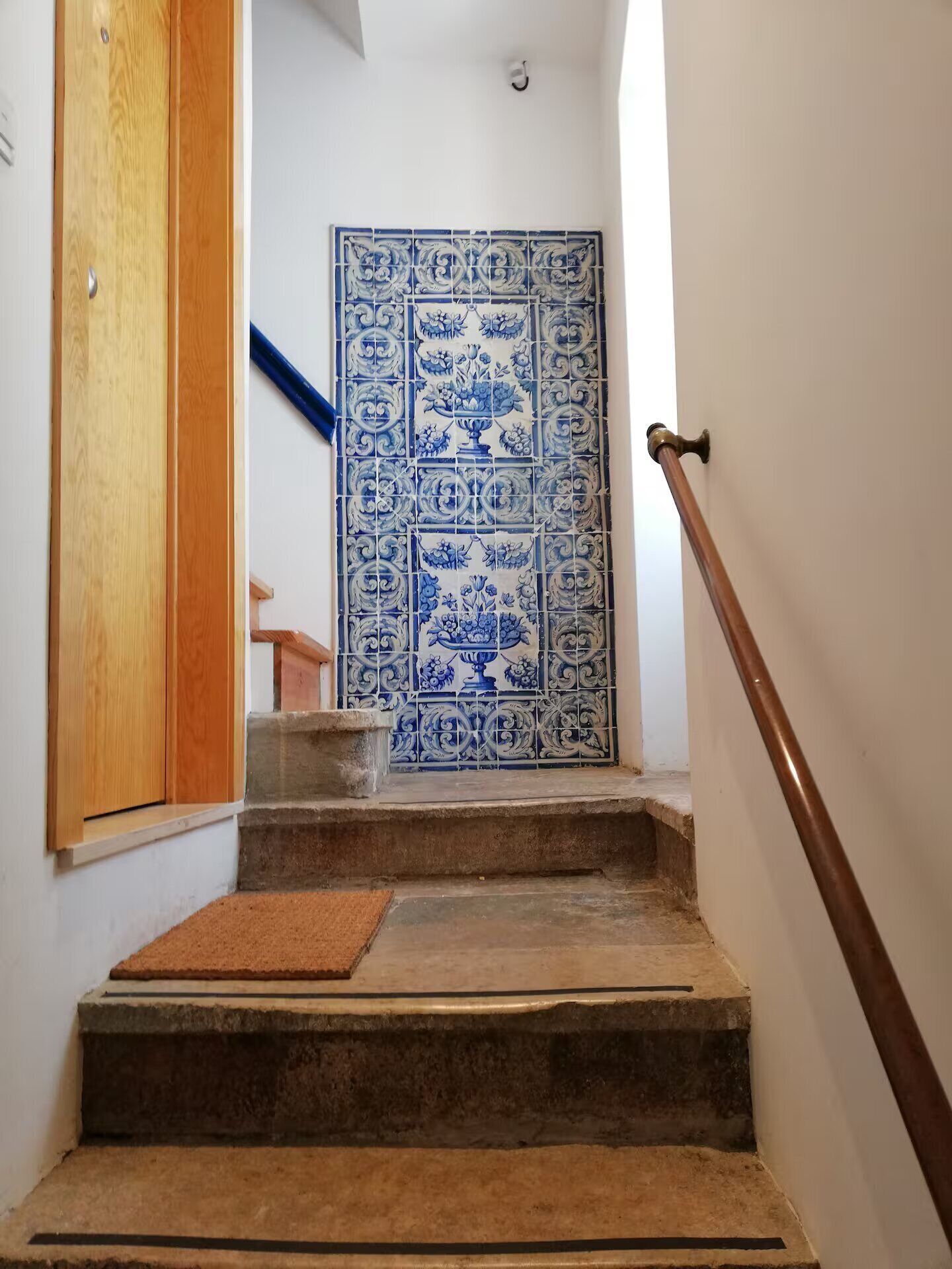 A staircase with a wooden handrail and a blue and white tiled wall at the top.