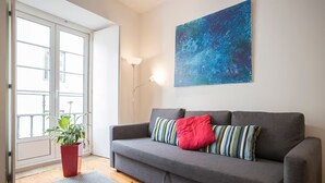 A modern living room with a grey sofa, a red plant, and a blue abstract painting on the wall.