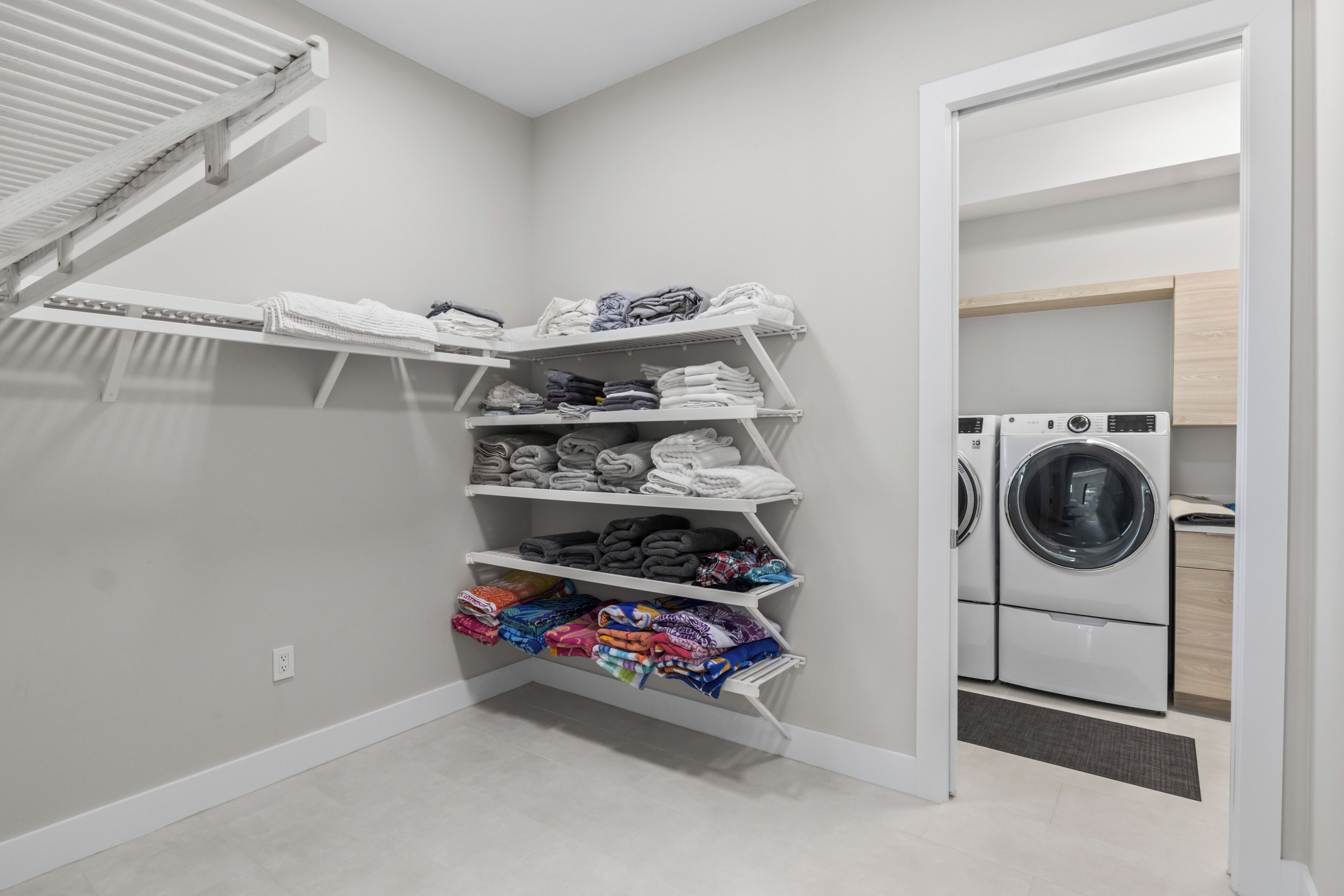 A laundry room with a built-in washer and dryer, a drying rack, and shelves for folded clothes.
