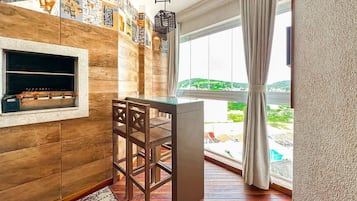 A cozy room with a wooden wall, a small bar area, and a large window with a view of greenery.