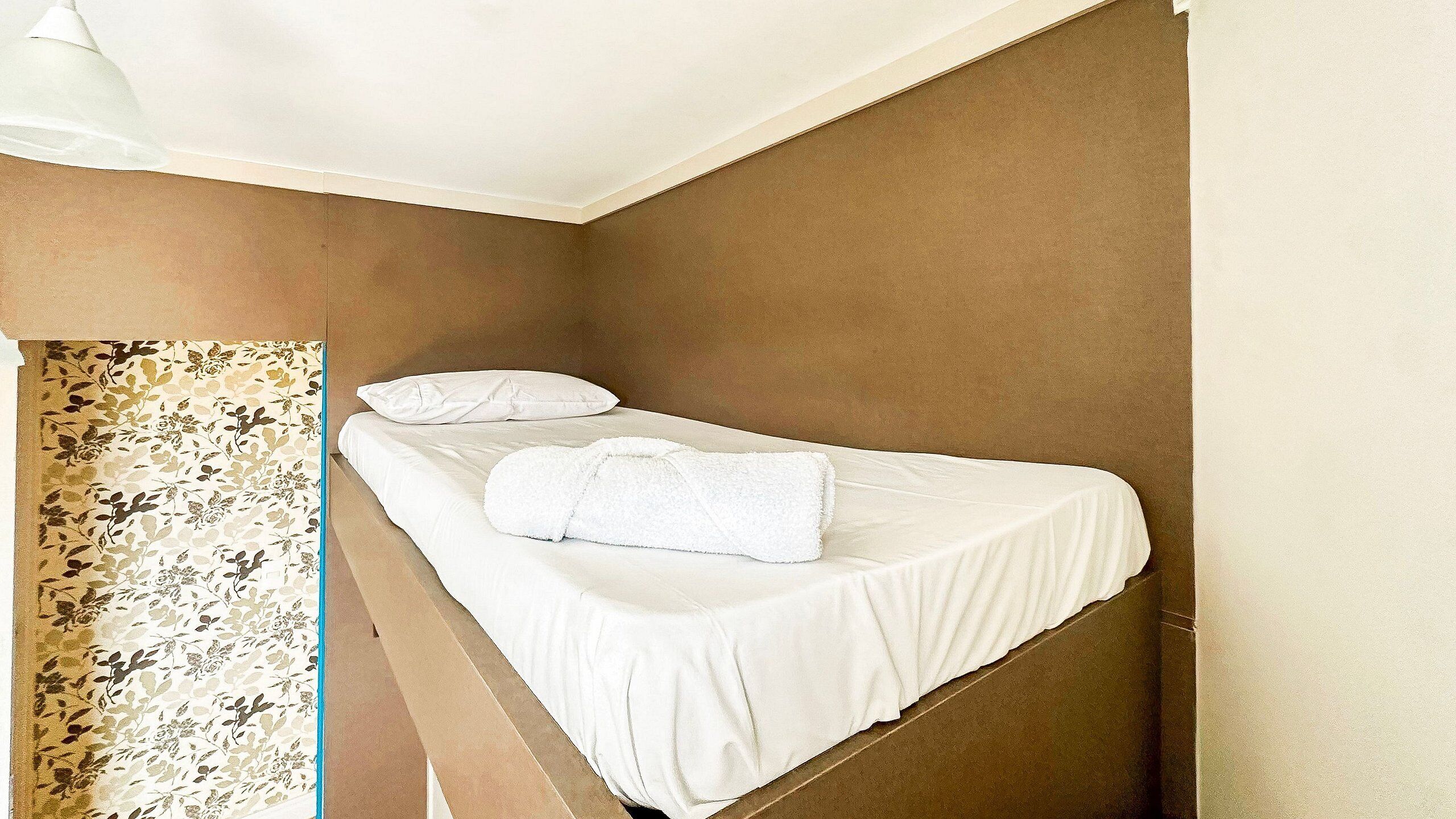 Una cama individual en una habitación de esquina con una colcha blanca y una toalla blanca.