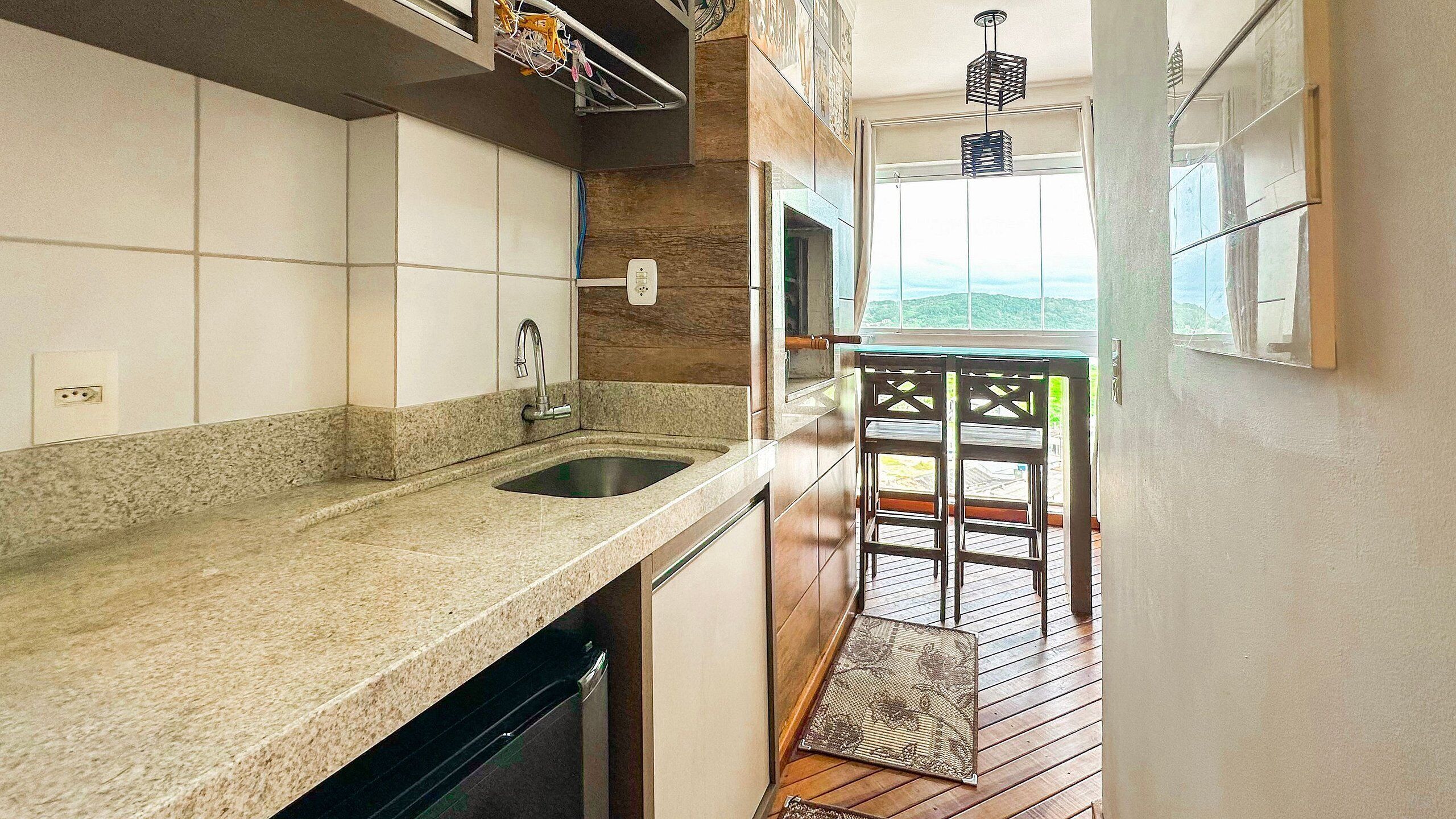 Una cocina con encimera de granito, pileta de acero inoxidable y piso de madera que da a un balcón con vistas.