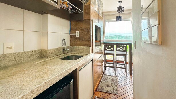 A kitchen with a granite countertop, a stainless steel sink, and a wooden floor leading to a balcony with a view. - Resid. Clube Mar Grosso-Laguna - LAG905 (Laguna)