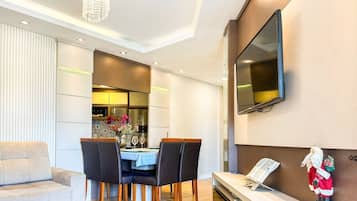 Una sala de estar moderna con comedor, un televisor de pantalla plana en la pared y una mesita con una figura de Santa Claus.