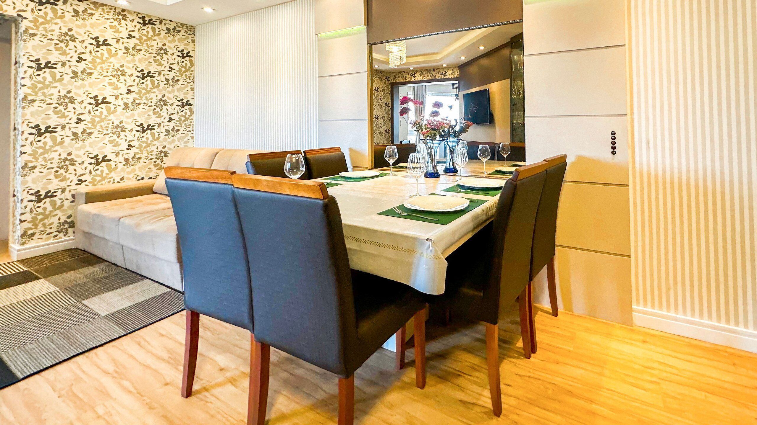 Uma área de refeições com uma mesa posta para quatro pessoas, rodeada por cadeiras estofadas azuis com pés de madeira.