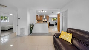 A modern living room with a brown leather sofa, a yellow pillow, and a kitchen area in the background.
