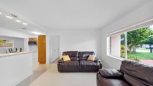 A modern living room with a brown leather sofa, a white reception desk, and a large window offering a view of the outdoors.