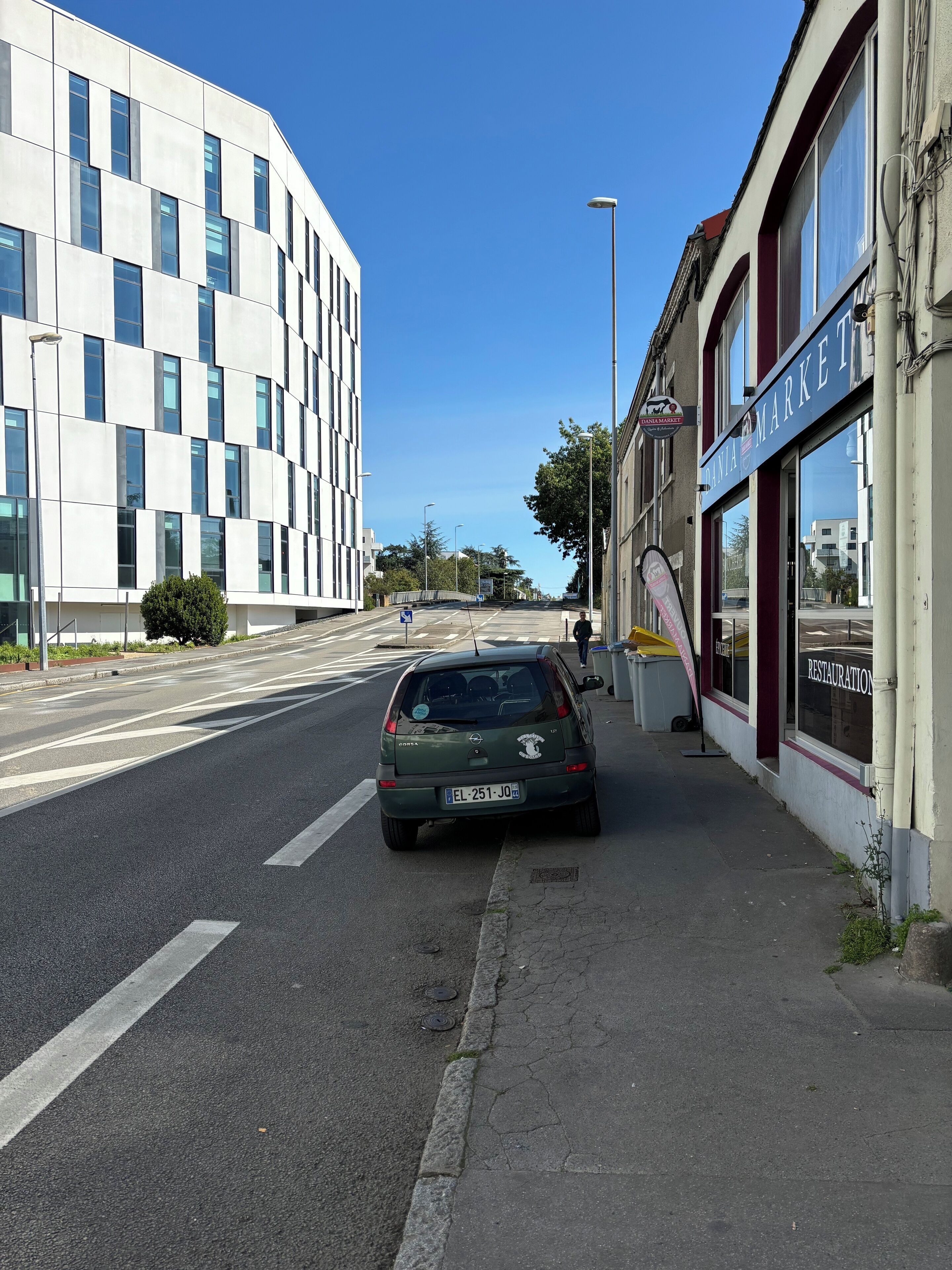 A car parked on a street with a building labeled "Banca Market" and a sign for "Restoration" on the right.