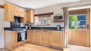A modern kitchen with wooden cabinets, a black countertop, and a built-in oven. There is a window with a view of greenery outside. - Inglewood, Kirkoswald - sleeps 4 guests  in 2 bedrooms (Kirkoswald)