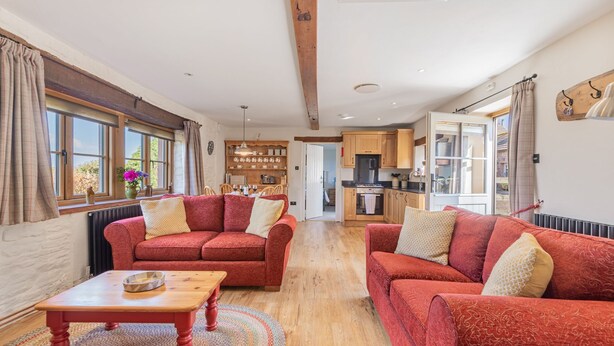 A spacious living room with two red sofas, a wooden coffee table, and a view of the kitchen and dining area. - Inglewood, Kirkoswald - sleeps 4 guests  in 2 bedrooms (Kirkoswald)