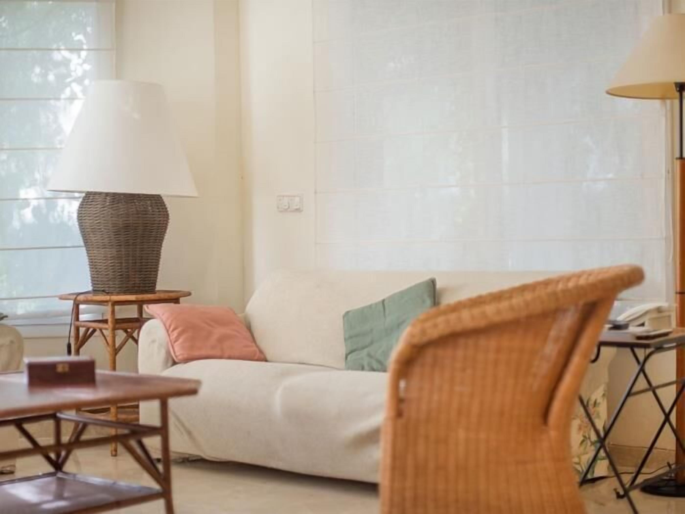 Een gezellige kamer met een bank, een rieten stoel, een tafeltje en een lamp.