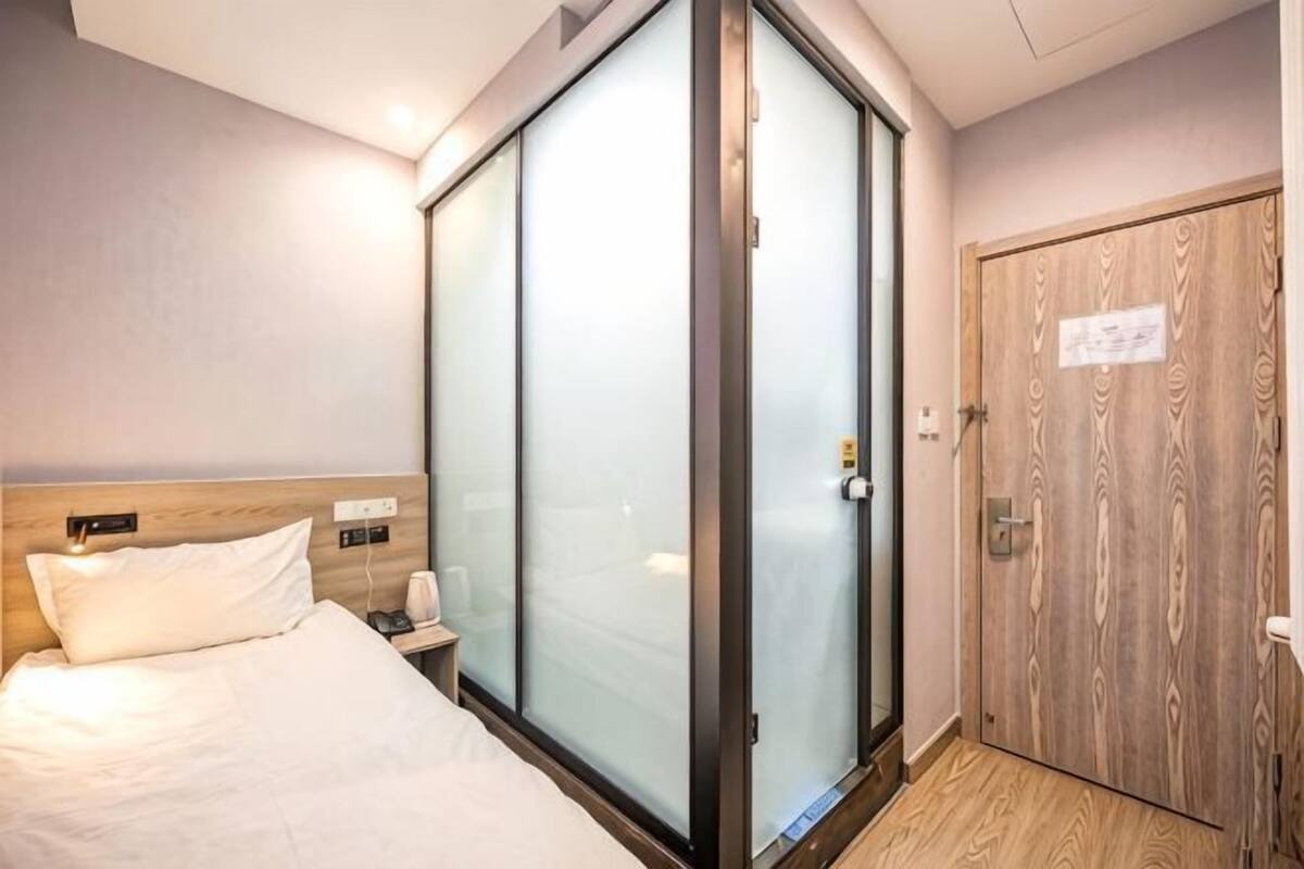 A hotel room with a bed, a nightstand, a wooden wardrobe, and a sliding glass door.