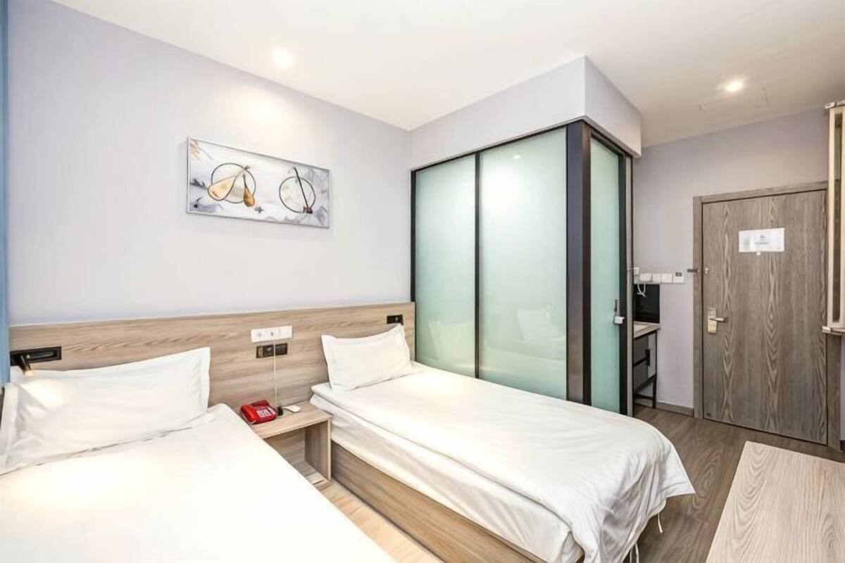 A hotel room with two beds, a wooden headboard, a glass partition, and a door with a sign.