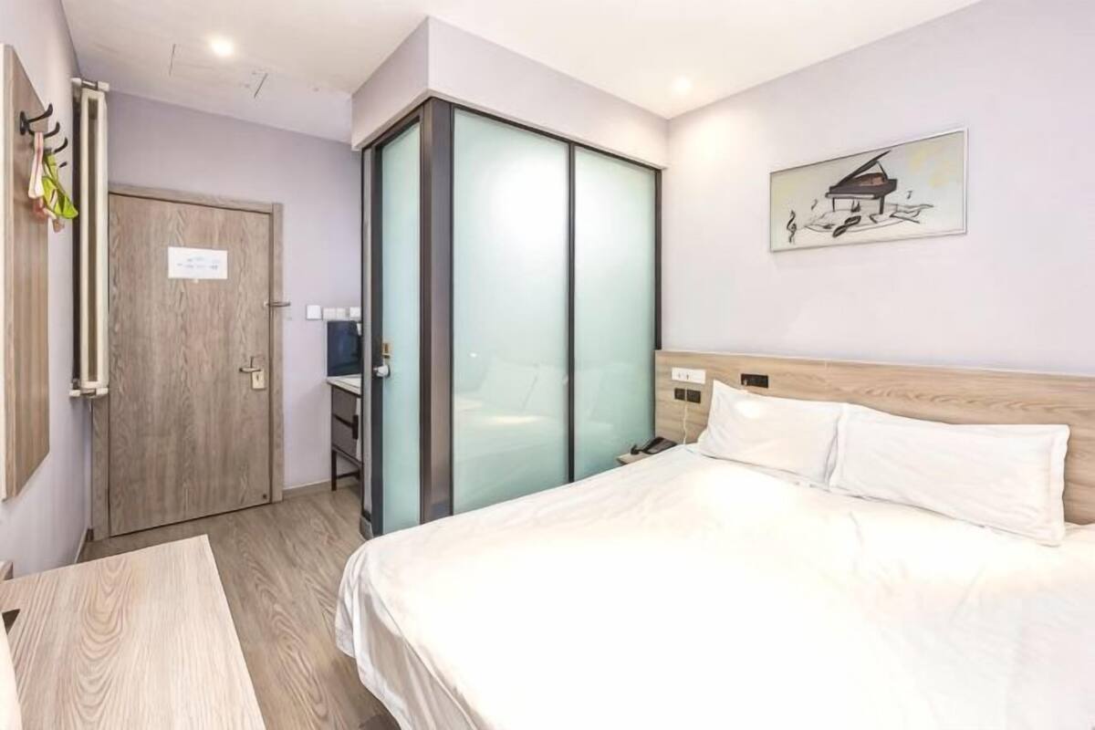 A hotel room with a bed, a wardrobe, a desk, and a painting on the wall.