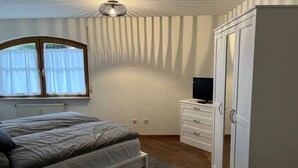 Ein Schlafzimmer mit einem Bett, einem Kleiderschrank, einem Fernseher und einem Fenster mit Vorhängen.