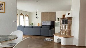 Ein modernes Wohnzimmer mit einem grauen Sofa, einem Holzschrank und einem Essbereich mit einem Glastisch und Stühlen.