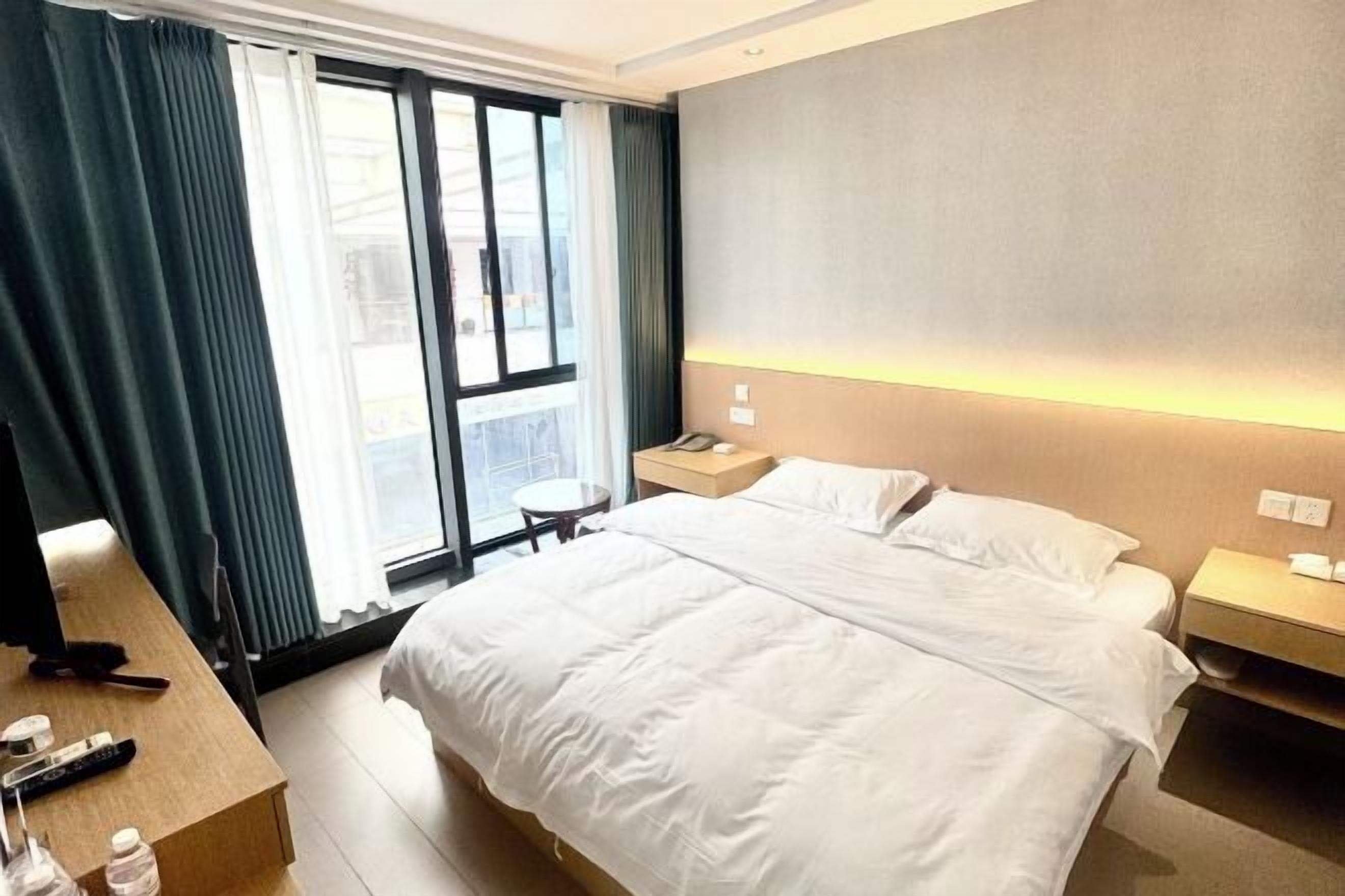 A hotel room with a bed, bedside tables, a desk, and a window with curtains.