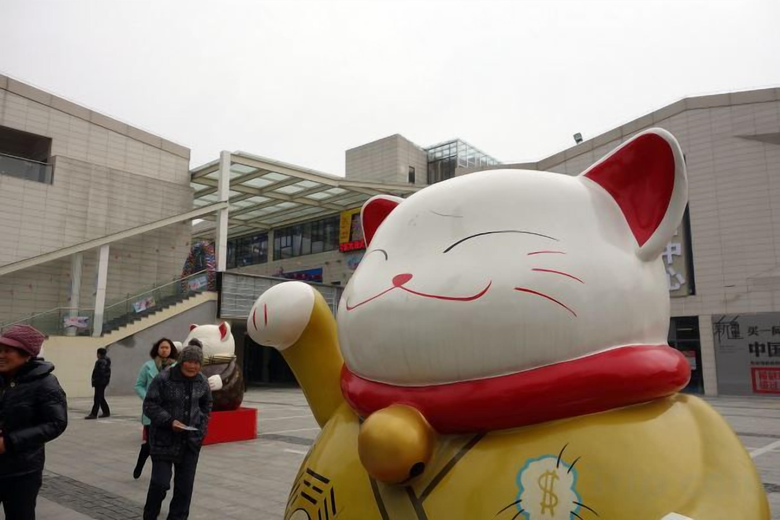 A large cat statue in an urban setting with modern architecture.