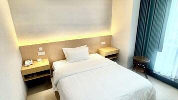 A hotel room with a bed, bedside tables, and a window with curtains.
