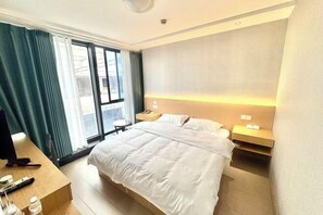 A hotel room with a large bed, a desk with a computer, a chair, and a window with curtains. - Yixing Hotel (Shanghai Zhujiajiao Ancient Town Scenic Area Branch) (Shanghai)