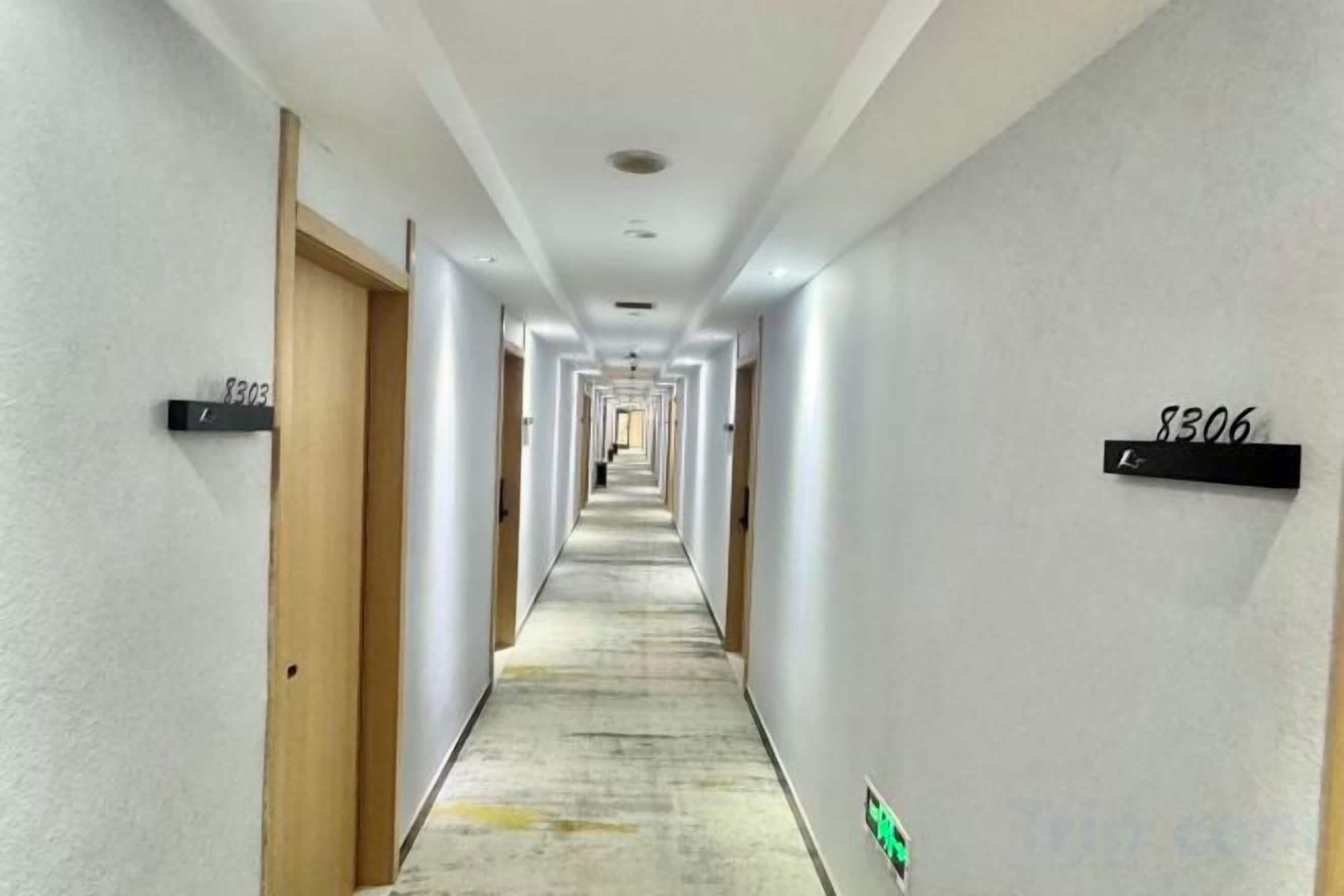 A long, narrow hotel corridor with doors on both sides, each marked with a number.
