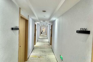 Un lungo e stretto corridoio d'albergo con porte su entrambi i lati, ognuna con un numero.