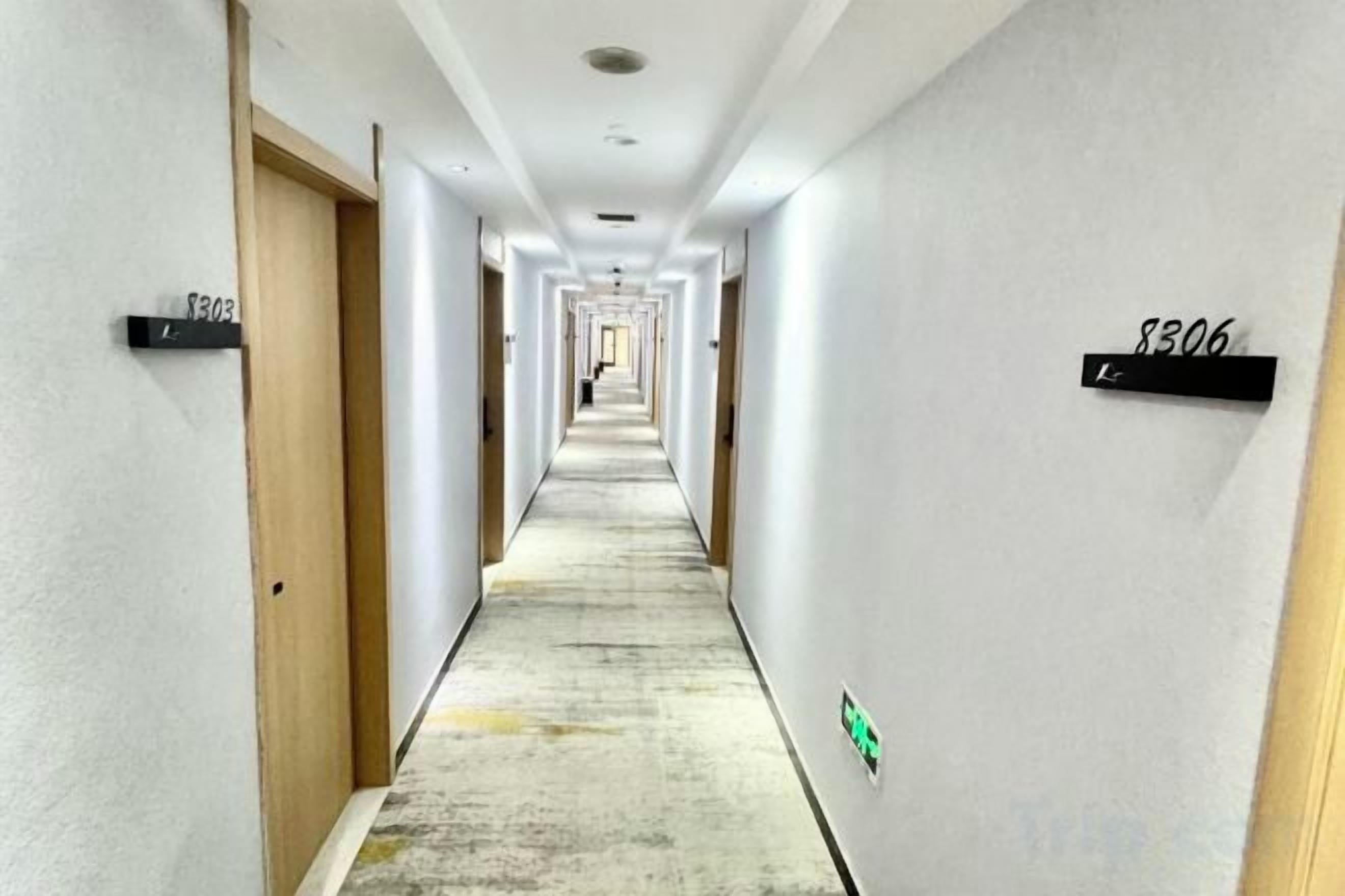 A long, narrow hotel corridor with doors on both sides, each marked with a number.
