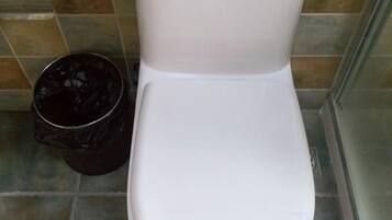 A white toilet next to a trash bin in a tiled bathroom.