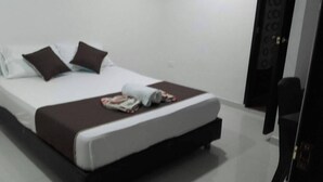 A neatly made bed with a white and brown bedspread, two dark brown pillows, and a folded white towel.