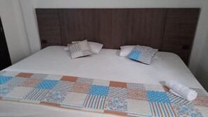A neatly made bed with a quilt and pillows, a wooden headboard, and a white wall.