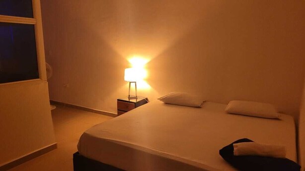 A hotel room with a bed, a bedside table, and a lamp.