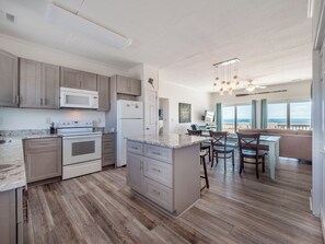 A modern kitchen with a central island, built-in appliances, and a dining area with a view of the ocean. - Green Dolphin by Topsail Realty (Holly Ridge)