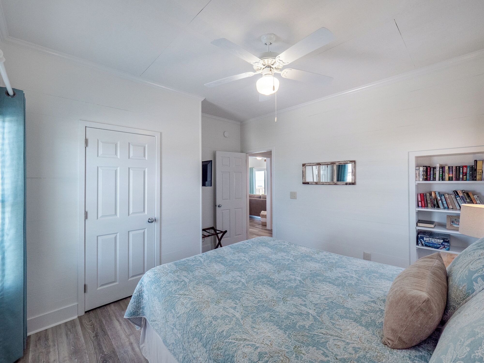 A bedroom with a bed, a ceiling fan, a bookshelf, and a door.