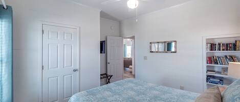 A bedroom with a bed, a ceiling fan, a bookshelf, and a door.