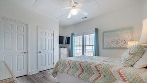A bedroom with a bed, a ceiling fan, a television, and a window with curtains. - Green Dolphin by Topsail Realty (Holly Ridge)