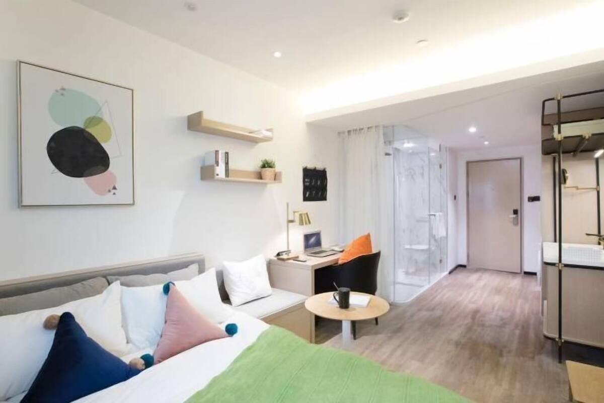 A modern hotel room with a bed, a desk, a chair, a small table, and a bathroom.