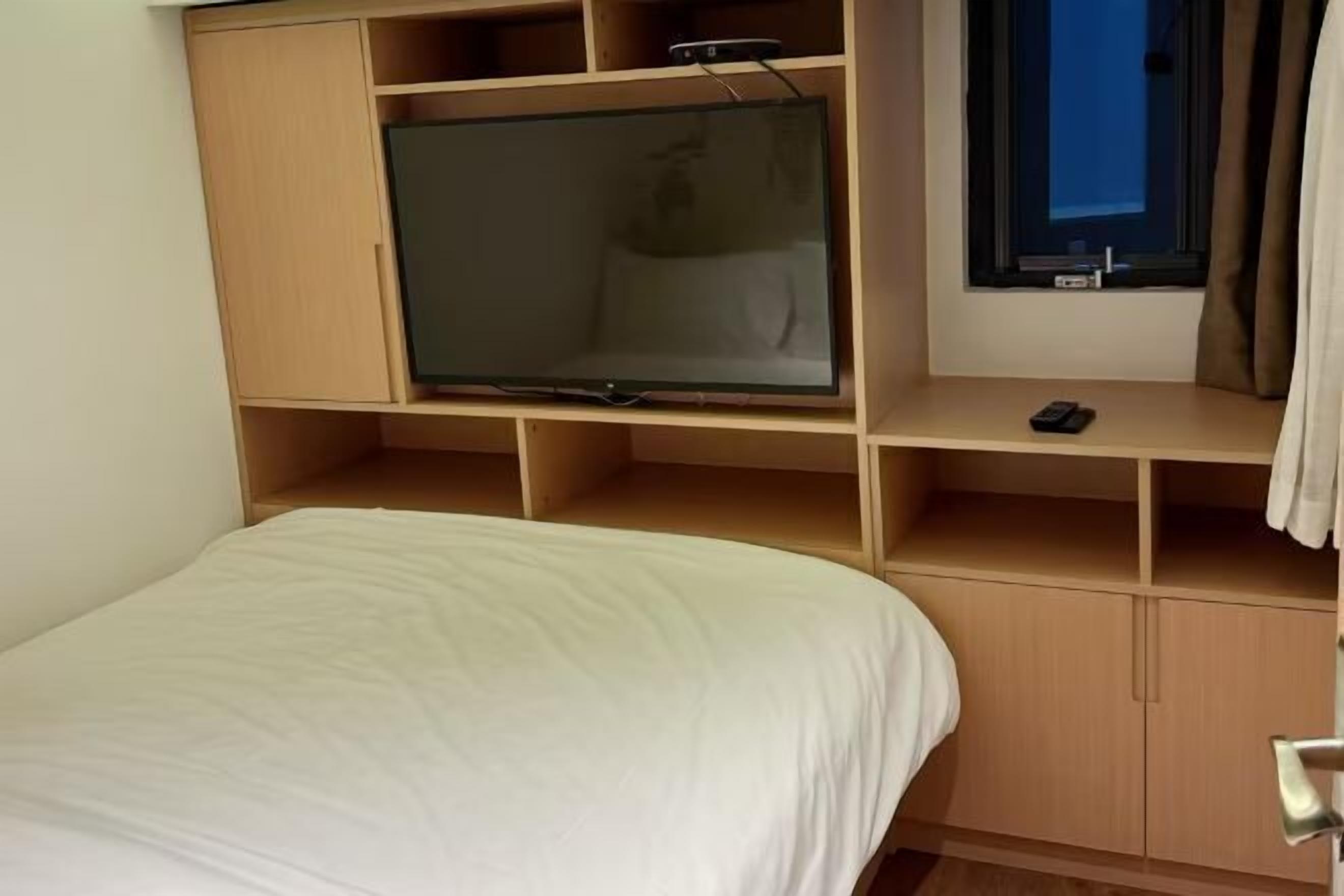 A bedroom with a bed, a TV, and a window with curtains.