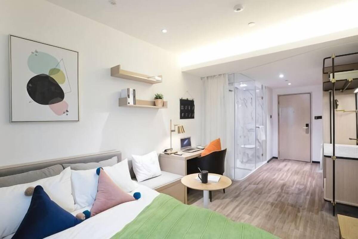 A modern hotel room with a bed, a desk, a chair, a small table, and a wardrobe.