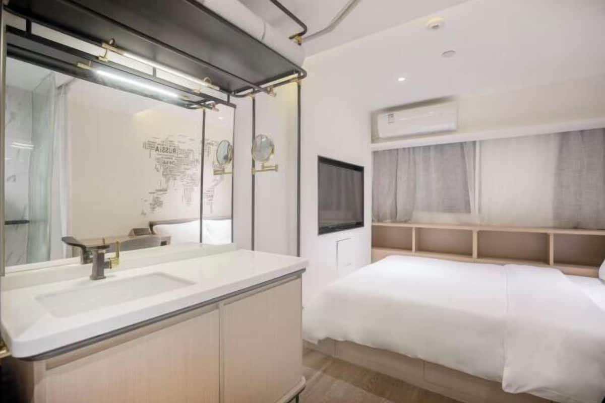 A modern hotel room with a large mirror, a sink, a bed, and a TV.