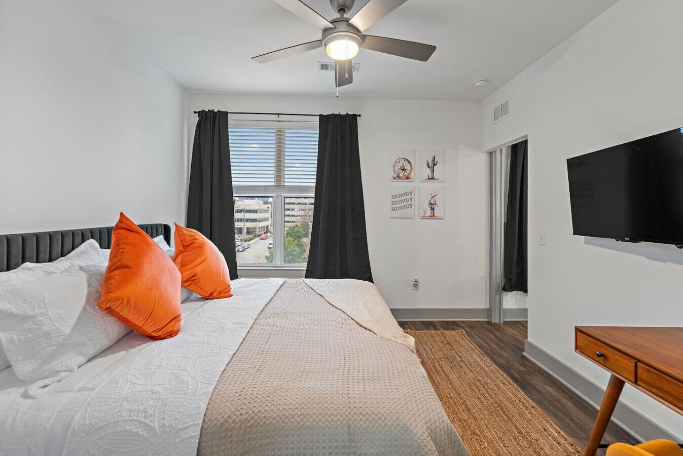 A hotel room with a bed, a ceiling fan, a TV, and a window with curtains.