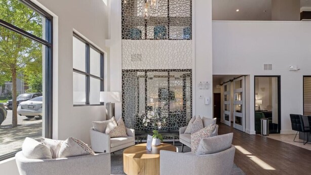 A modern lobby with a high ceiling, a seating area with two sofas and a coffee table, and a decorative wall with a mosaic pattern. - Mid-Century Charm | Midtown (Nashville)